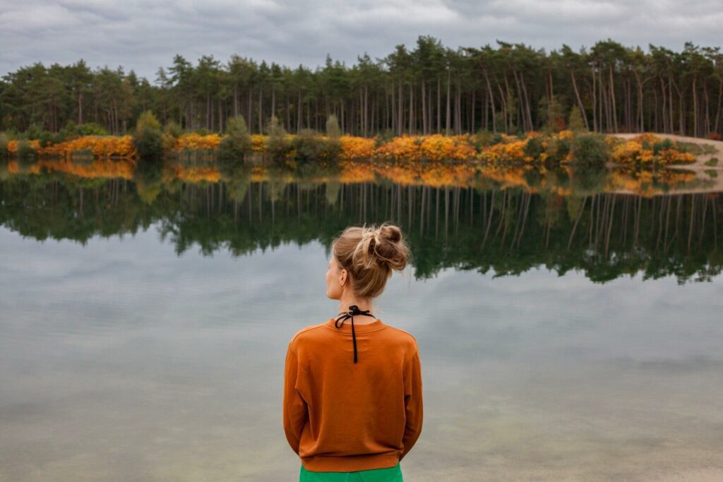 Person looking at their reflection in a calm woodland lake, representing how perception can influence body image