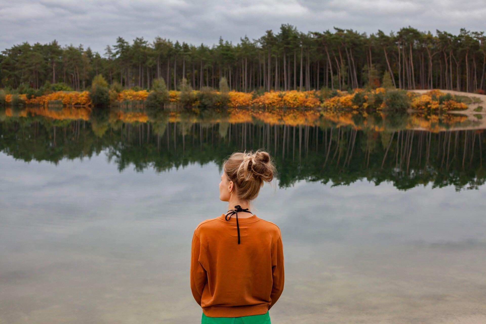 Person looking at their reflection in a calm woodland lake, representing how perception can influence body image